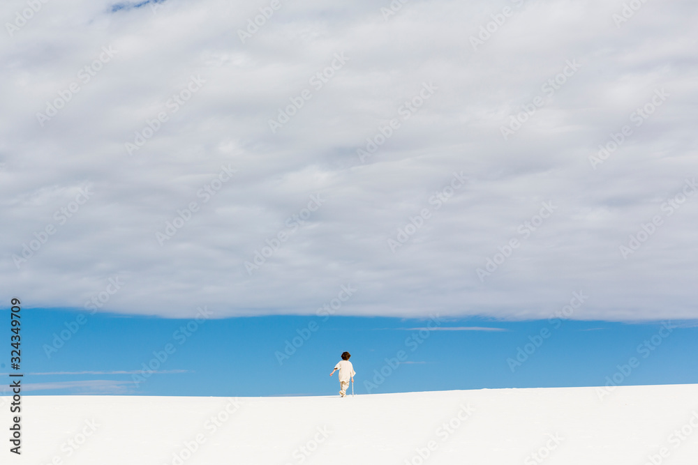 6 year old boy walking in white sand dunes, a strip of blue sky on the horizon and thick cloud. ,White Sands National Monument 6 year old boy walking in white sand dunes, a strip of blue sky on the horizon and thick cloud. ,White Sands National Monument