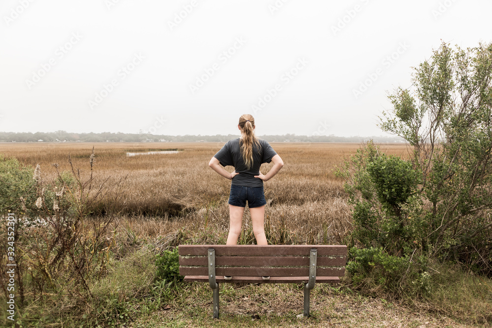 Teenage girl standing on a bench looking out over marshes, St. Simon's Island, Georgia,St Simon's Island Teenage girl standing on a bench looking out over marshes, St. Simon's Island, Georgia,St Simon's Island