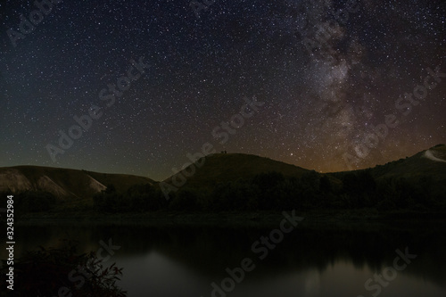 Milky Way stars in the sky. Night landscape with hills by the river.