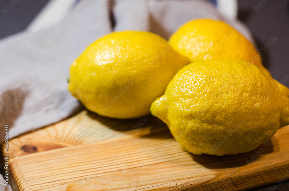 Three fresh yellow lemons lie on a wooden cutting Board along with a grey linen napkin. Selective focus. Close up.