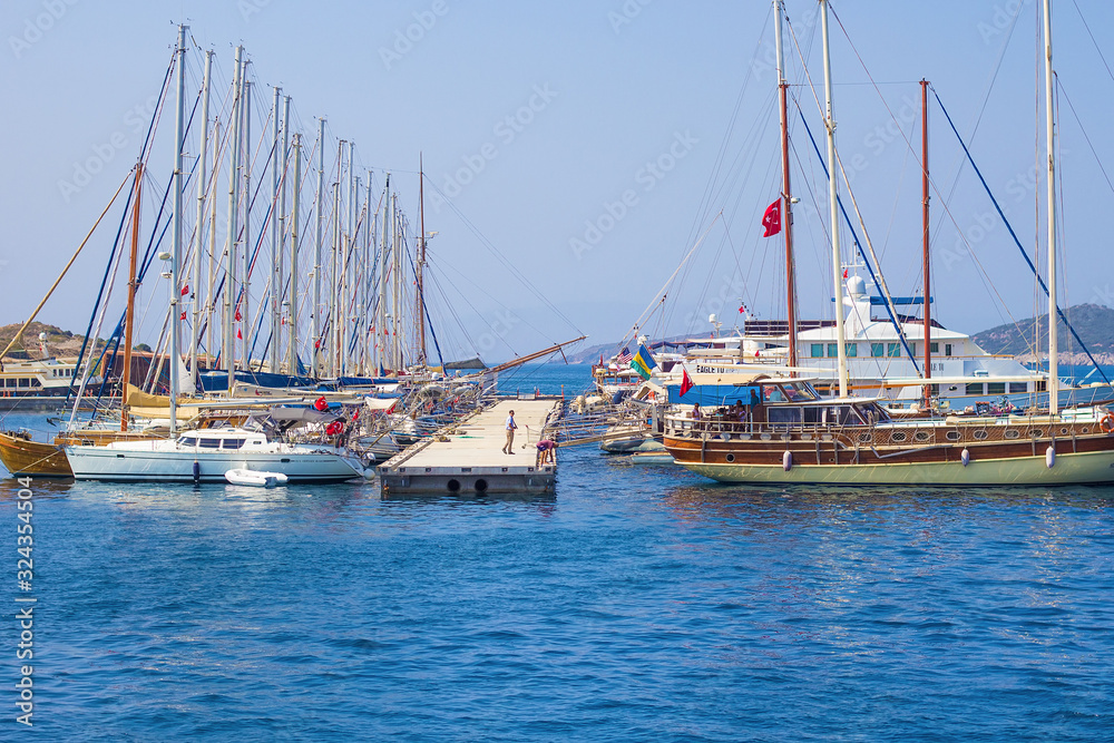 View on luxury yachts, ships and sailing boats near the shores of blue Aegean sea, moored on Bodrum port, Mugla, Turkey. Turkish summer vacation, water activity