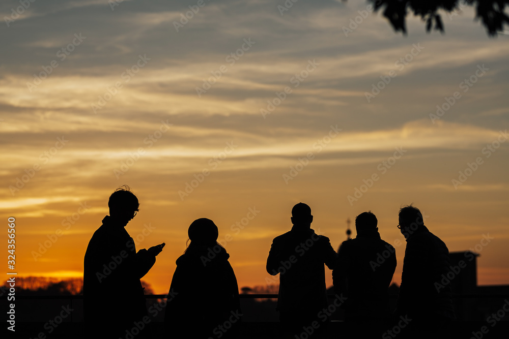 FLORENCE, ITALY - MARCH 05, 2019: Silhouettes of people taking pictures of the sunset with mobile phones and selfie stick on a sunset in Florence, Italy. Rear view.