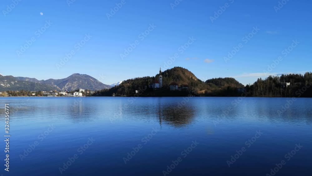 Wide shot lake Bled island Catholic church with waves on water surface, Slovenia