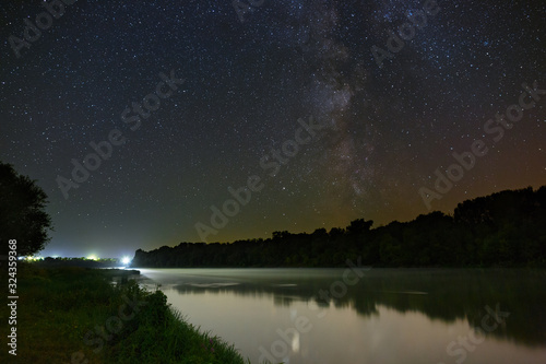 Milky Way stars in the sky above the river. Night landscape photographed with a long exposure. © olgapkurguzova