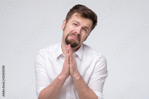 Emotive guy clenching hands together frowning while begging for forgiveness