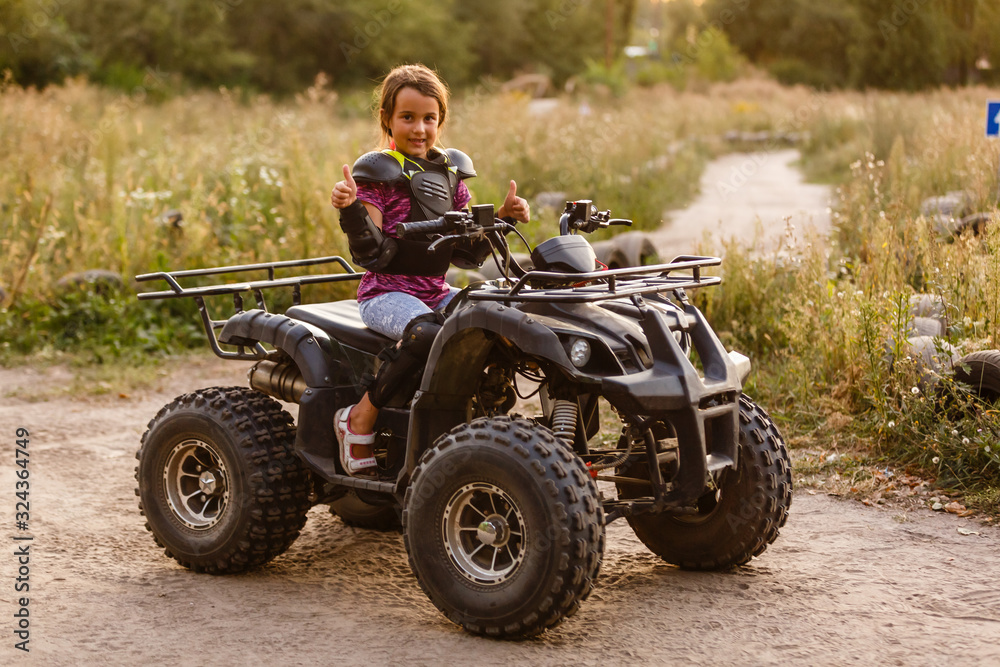 Happy little girl playing on road at the day time. He driving on quad bike in the park. Child having fun on the nature. Concept of happiness. Happy little girl playing on road at the day time. He driving on quad bike in the park. Child having fun on the nature. Concept of happiness.