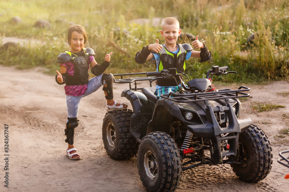 Happy little children playing on road at the day time. They driving on quad bike in the park. Kids having fun on the nature. Concept of happiness.