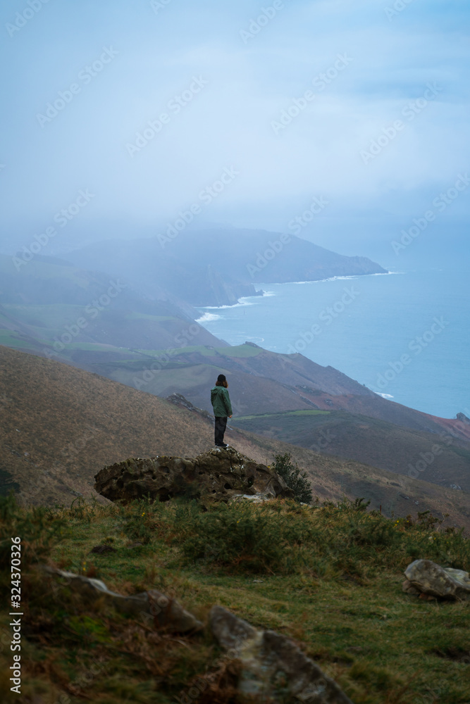 Man standing on top of a big rock contemplating the views from the top of Basque Country coast