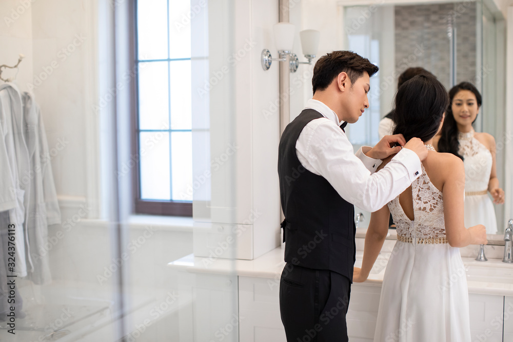 Happy young Chinese man helping wife getting dressed Happy young Chinese man helping wife getting dressed