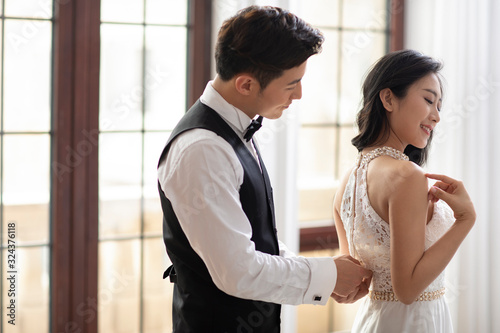 Happy young Chinese man zipping up wife's dress at home