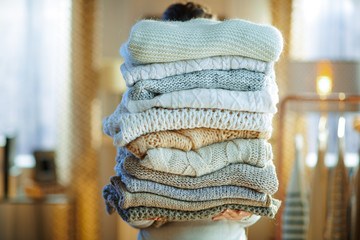 woman in modern house in sunny winter day holding huge sweaters