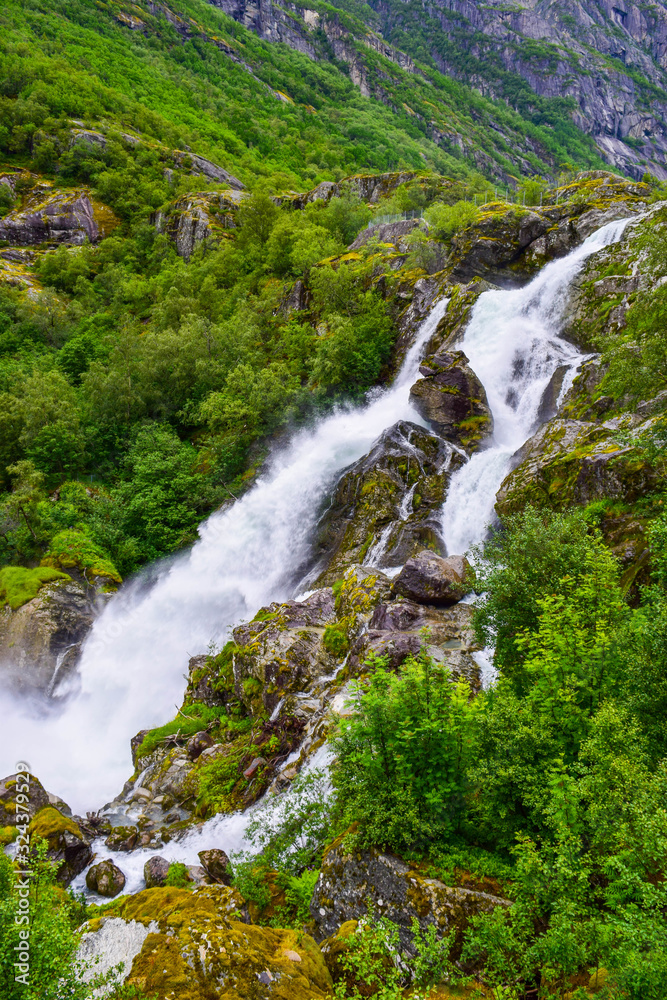 Waterfall and river which is located near path to the Briksdalsbreen (Briksdal) glacier. The melting of this glacier forms waterfall and river with clear water. Jostedalsbreen National Park. Norway.