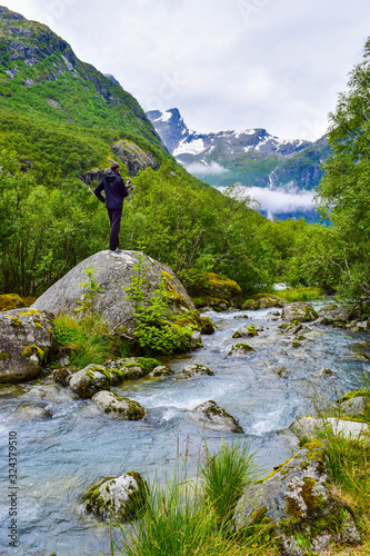 Tourist near river which is located near path to the Briksdalsbreen (Briksdal) glacier. The melting of this glacier forms waterfall and river with clear water. Jostedalsbreen National Park. Norway. photo