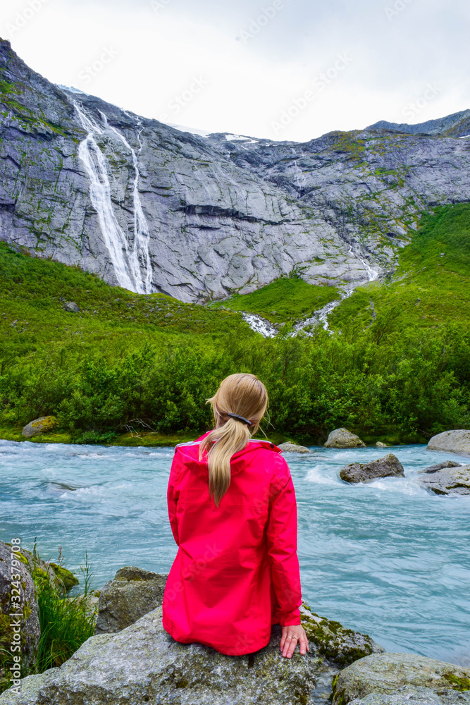 The young woman near river which is located near path to the Briksdalsbreen (Briksdal) glacier. The melting of this glacier forms waterfall and river with clear water. Jostedalsbreen National Park. No The young woman near river which is located near path to the Briksdalsbreen (Briksdal) glacier. The melting of this glacier forms waterfall and river with clear water. Jostedalsbreen National Park. No