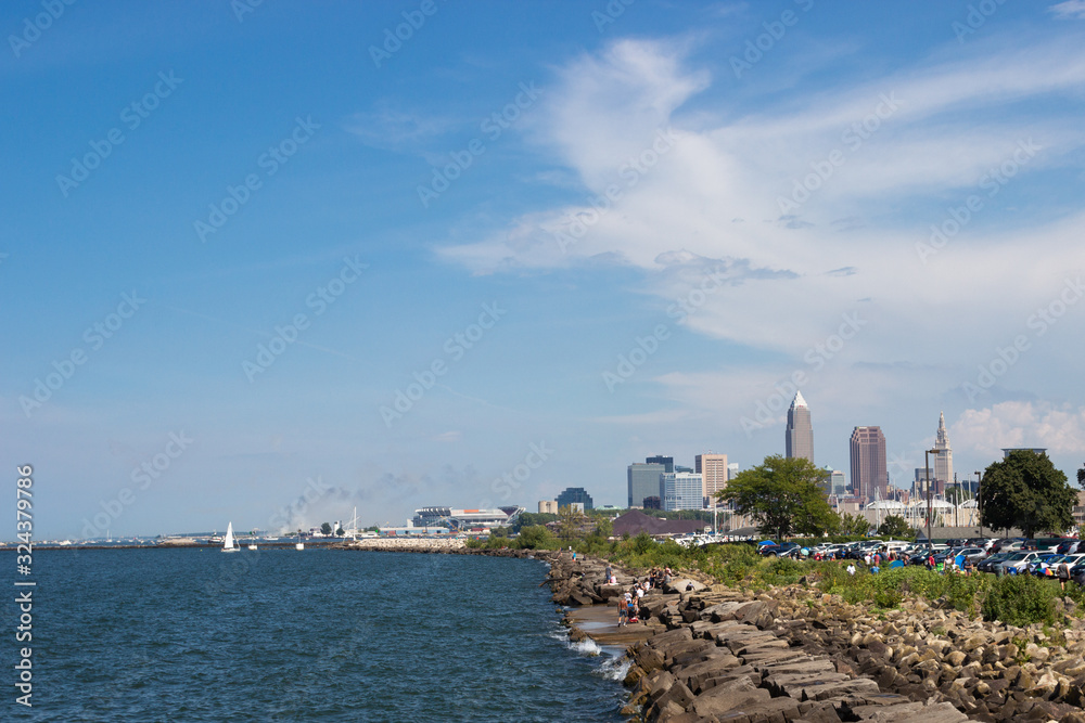 Fototapeta premium Beautiful summer landscape, which depicts the rocky shore of the lake, waves on the water and in the distance are the pain of skyscrapers. View of city of Cleveland,Ohio,USA from the lake Erie