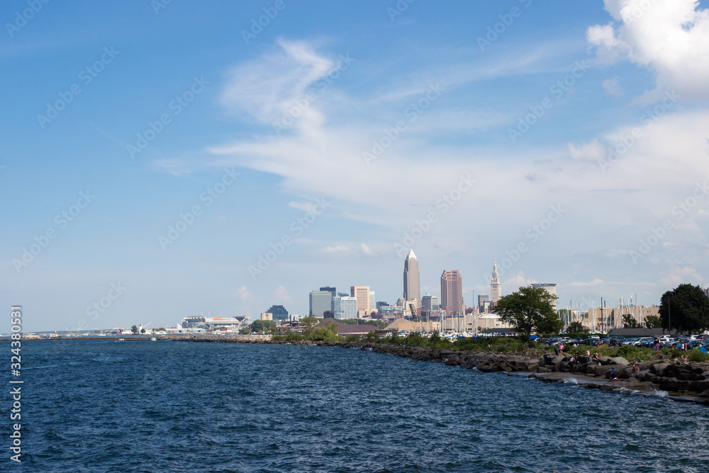 Naklejka premium Beautiful summer landscape, which depicts the rocky shore of the lake, waves on the water and in the distance are the pain of skyscrapers. View of city of Cleveland,Ohio,USA from the lake Erie