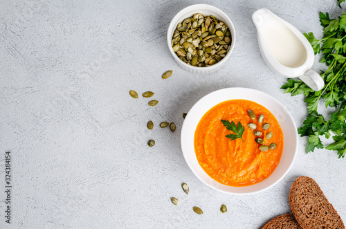 Vegetarian autumn cream soup of pumpkins and carrots with seeds and parsley on a gray background with copy space, flat lay