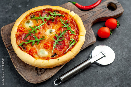 tasty Italian pizza with tomato, cheese, quail eggs sausage on a cutting board on a stone background