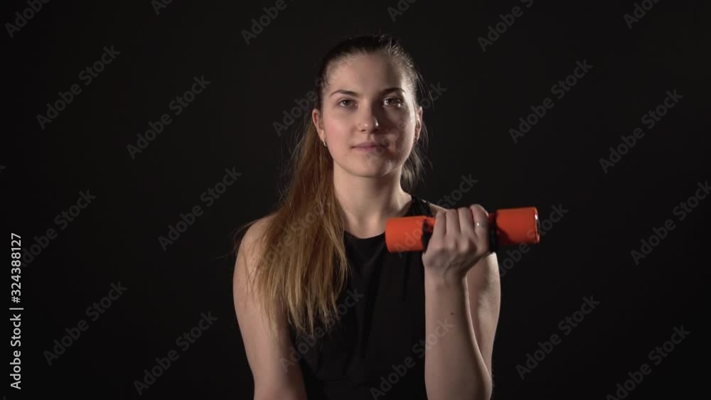 The girl shakes her biceps, dumbbells on a black background, advertising for fitness