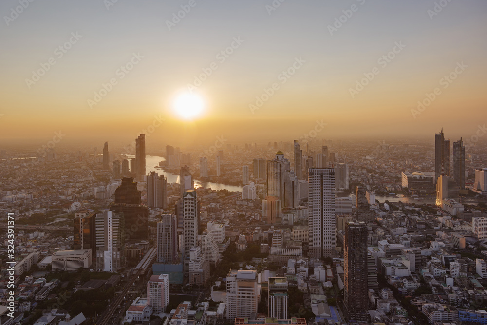 Aerial silhouette view cityscape of Bangkok, buildings along Chao Phraya river, with golden and blue dramatic twilight sky against sun in sunset with air pollution of pm 2.5 from Mahanakorn Tower.