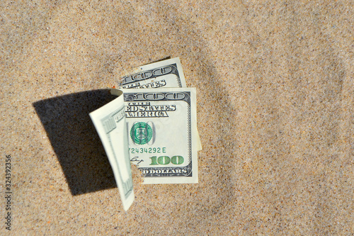 Money dolars half covered with sand lie on beach close-up photo