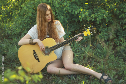Woman wearing a white knitted blouse and beige shorts in nature with a guitar.