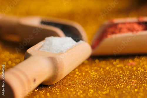 small wooden spoons with black sesame, salt and papic on a yellow shiny background
