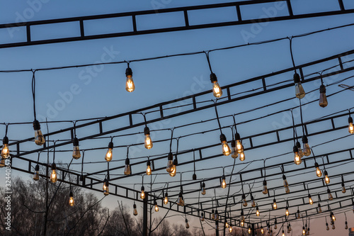 lamps / garlands shine over the evening cafe against the blue sky © Volodymyr