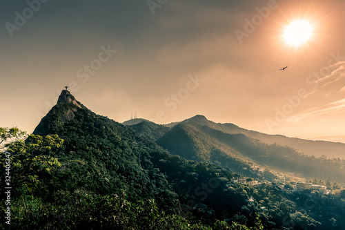 Christ the Redeemer (Cristo Redentor) on Mount Corcovado during beautiful sunset with mountains & trees from Tijuca National Park & a bird flying past the sun in Rio de Janeiro, Brazil, South America