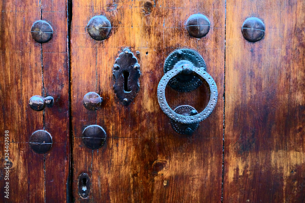 Beautiful old wooden door, a lock, a knob, and a wrought iron door knocker, hard contrast light. Beautiful old wooden door, a lock, a knob, and a wrought iron door knocker, hard contrast light.
