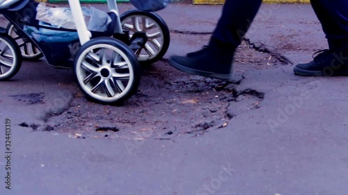 A woman with a stroller and a child rides on a destroyed road. Not a repaired road. Pit on the pavement.