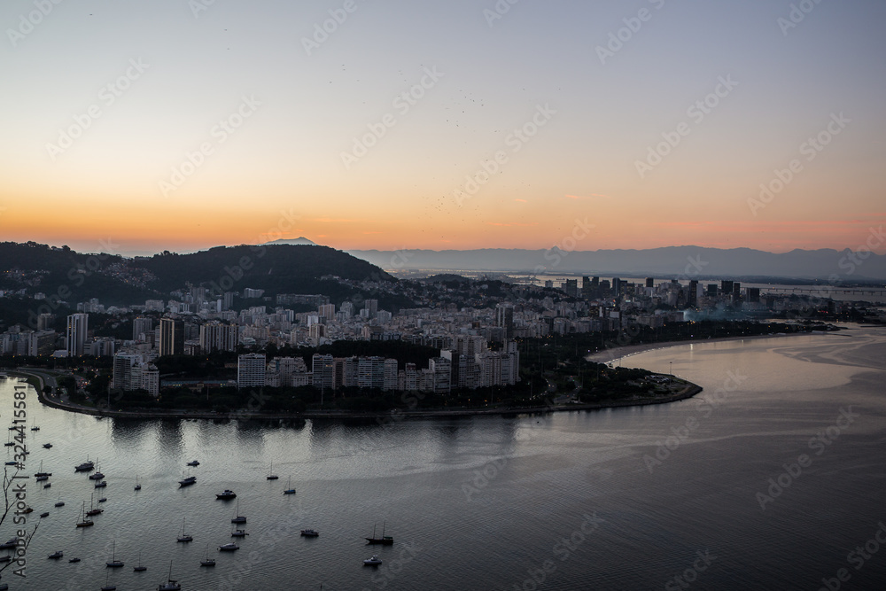 Sunset view over Guanabara Bay from Sugarloaf mountain in Urca towards city of Rio de Janeiro with boats in bay & mountains in background with a warm summer sky overhead in Rio, Brazil, South America