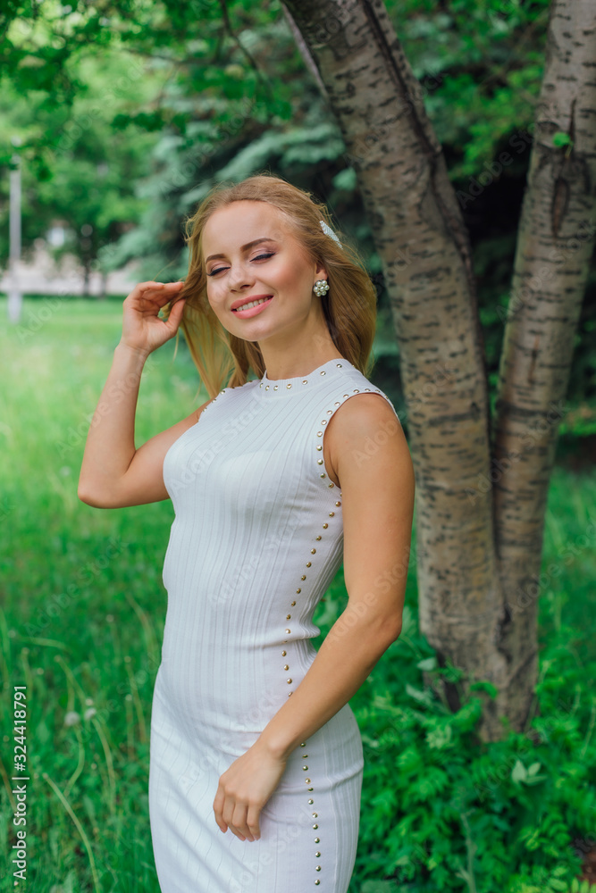Portrait of a charming blond woman wearing beautiful white dress standing next to rowan tree. Portrait of a charming blond woman wearing beautiful white dress standing next to rowan tree.