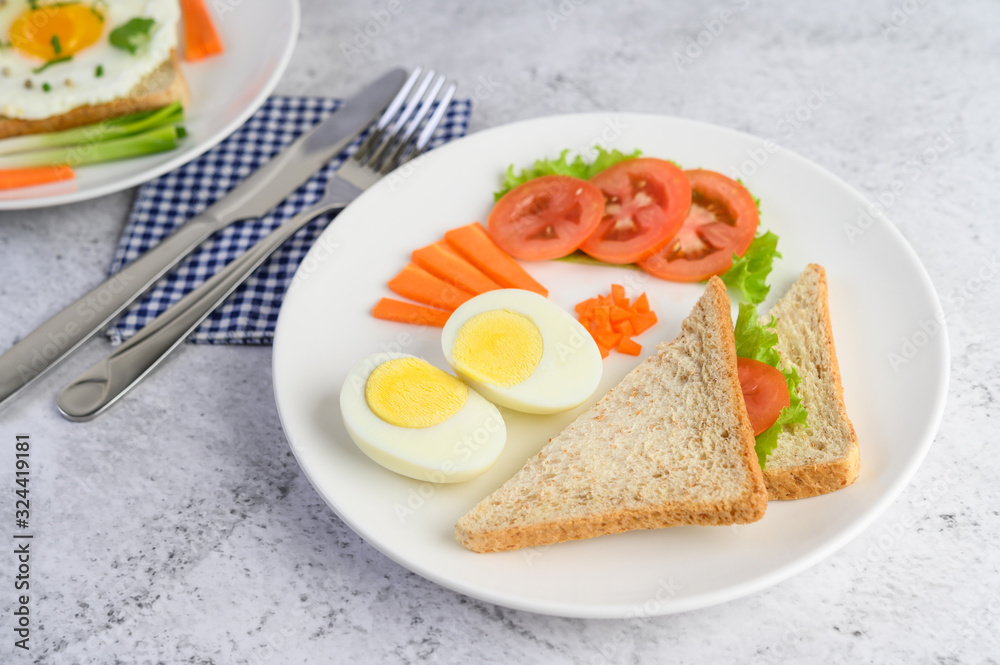 Boiled eggs, bread, carrots, and tomatoes on a white plate with a knife and fork. Boiled eggs, bread, carrots, and tomatoes on a white plate with a knife and fork.