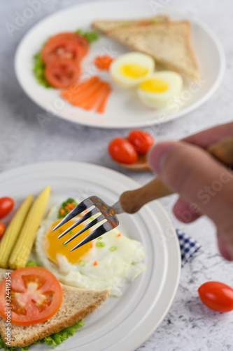 Fried eggs, bread, carrots and tomatoes on a white plate for breakfast, Selective focus handheld with a fork.