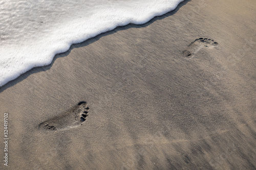 Footprints on sand about to get washed by the waves photo