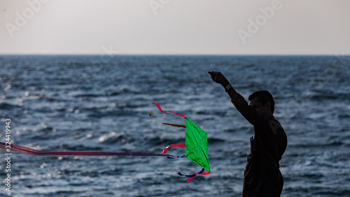 A man silhoetted against the shore waters tries to fly a home made kite photo
