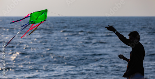 A man silhoetted against the shore waters tries to fly a home made kite photo