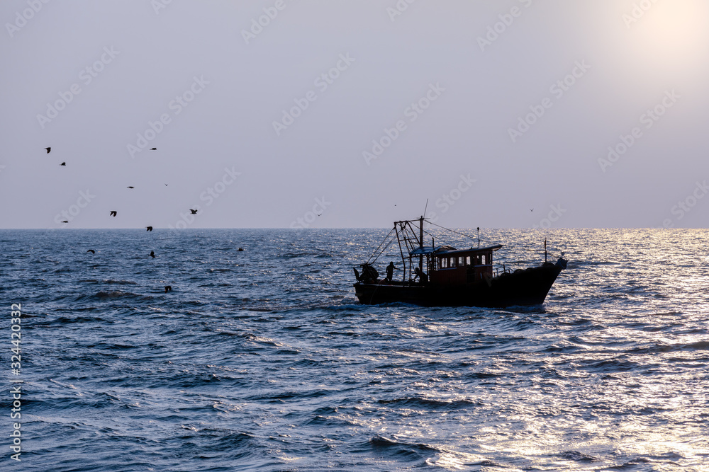 A fishing trawler returning after a day's catch is silhoetted agaist the evening sun in Kerala, India