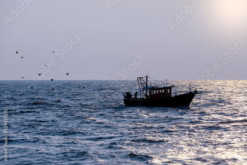 A fishing trawler returning after a day's catch is silhoetted agaist the evening sun in Kerala, India photo