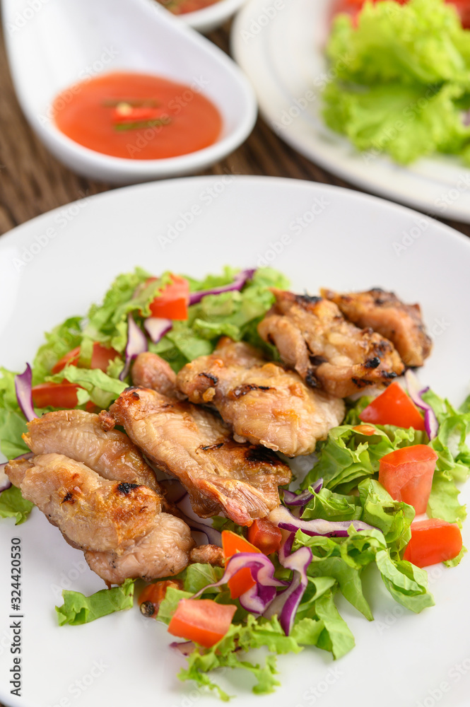 Grilled chicken on a white plate with a salad of tomatoes, carrots and chilies cut into pieces.