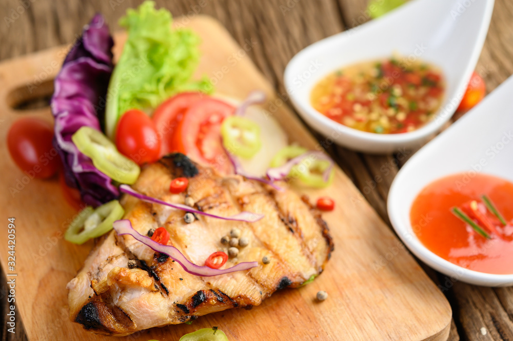 Grilled chicken on a Wood cutting board with salad, tomatoes, chilies cut into pieces, and sauce. Grilled chicken on a Wood cutting board with salad, tomatoes, chilies cut into pieces, and sauce.