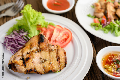Grilled chicken on a white plate with a salad of tomatoes, carrots and chilies cut into pieces.