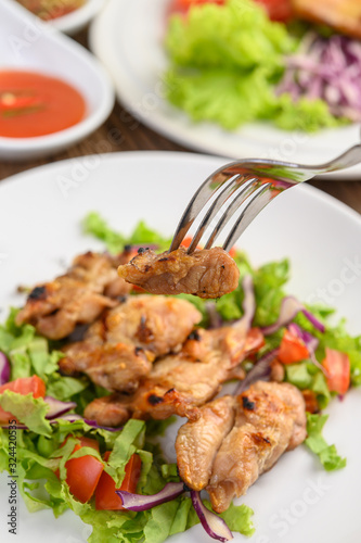Grilled chicken on a white plate with a salad of tomatoes  carrots and chilies cut into pieces.