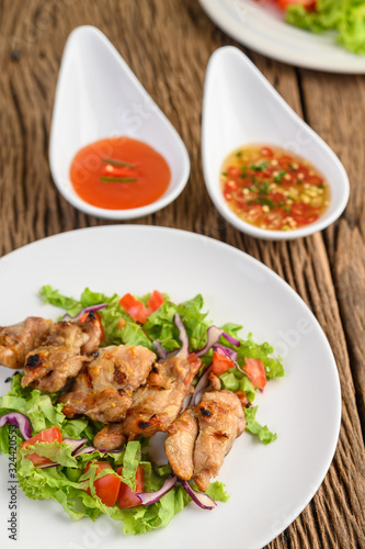 Grilled chicken on a white plate with a salad of tomatoes, carrots and chilies cut into pieces.