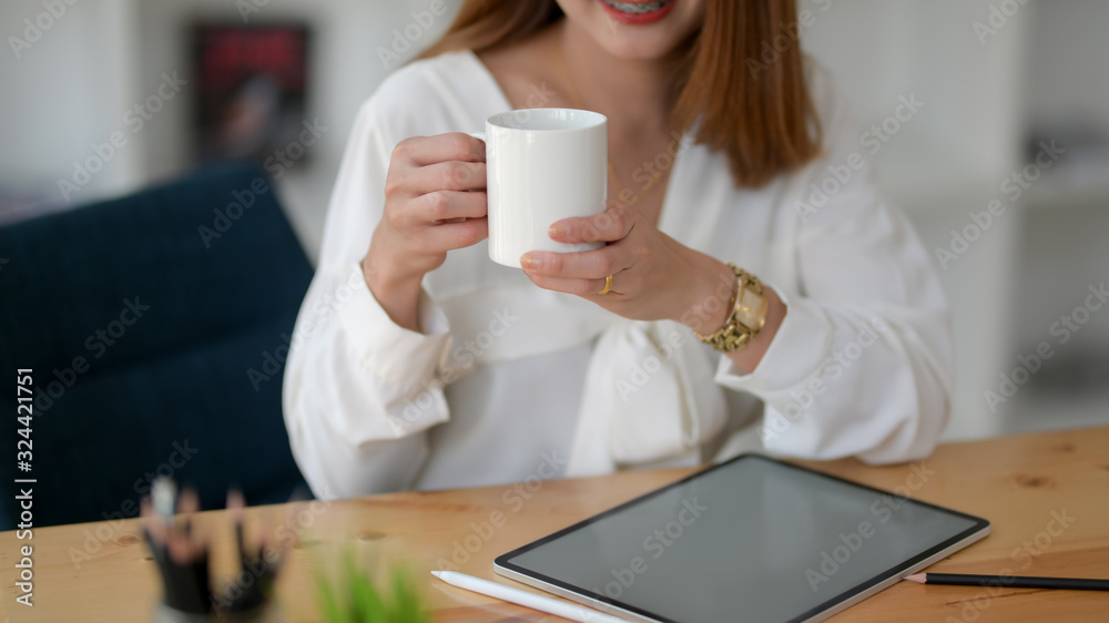 Close up view of freelancer holding a coffee cup while working with digital tablet Close up view of freelancer holding a coffee cup while working with digital tablet