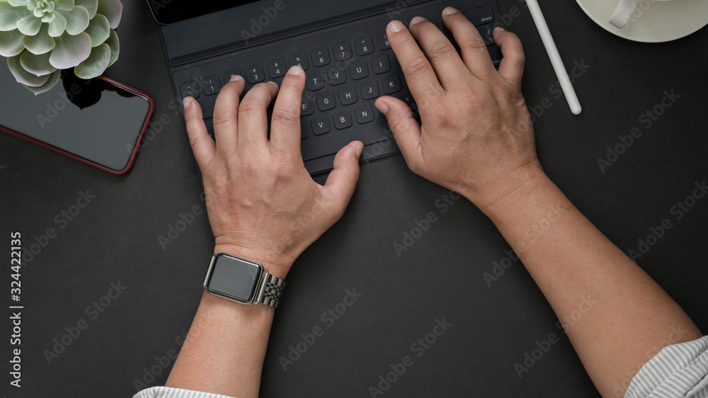 Overhead shot of male freelancer typing on wireless keyboard in dark modern workspace Overhead shot of male freelancer typing on wireless keyboard in dark modern workspace