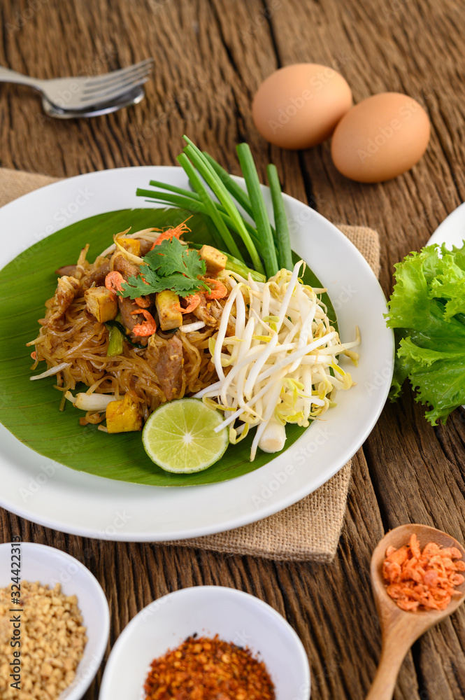 Pad Thai in a white plate with lemon, eggs and seasoning on a wooden table. Pad Thai in a white plate with lemon, eggs and seasoning on a wooden table.