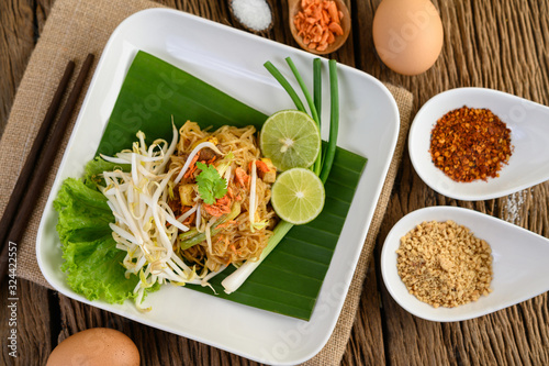 Pad Thai in a white plate with lemon, eggs and seasoning on a wooden table.