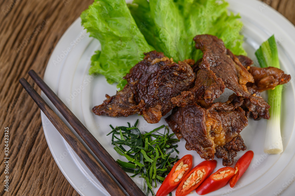 Beef fried Thai food on a white plate with spring onion, kaffir lime leaves, chilies, chopsticks, salad and chili paste in a cup.